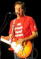 McCartney, in his late sixties, playing an orange electric guitar and
